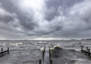 Wooden jetty on the shore of a lake with an approaching thunderstorm on the horizon. Black and white image.